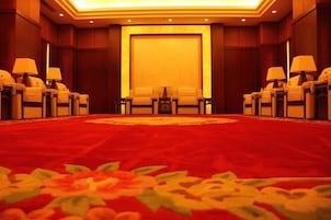 Un salón de conferencias con piso alfombrado, filas de sillas y mesas con lámparas.