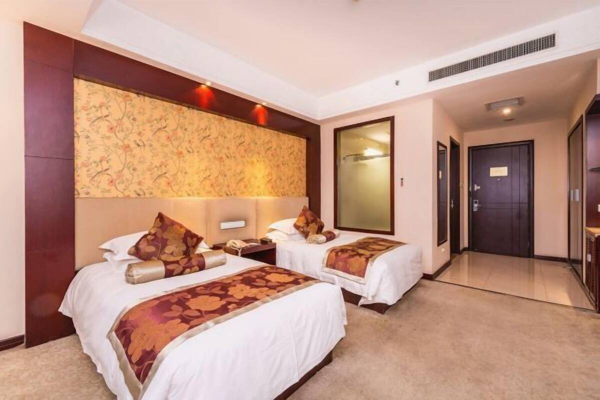 Quarto de hotel com duas camas, um espelho grande e piso coberto de carpete.