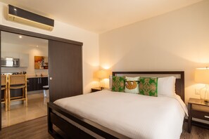 A hotel room with a bed, bedside lamps, a wooden headboard, and a view of the kitchen area. - Reserva Conchal Resort - Roble Sabana Complex (Cabo Velas)