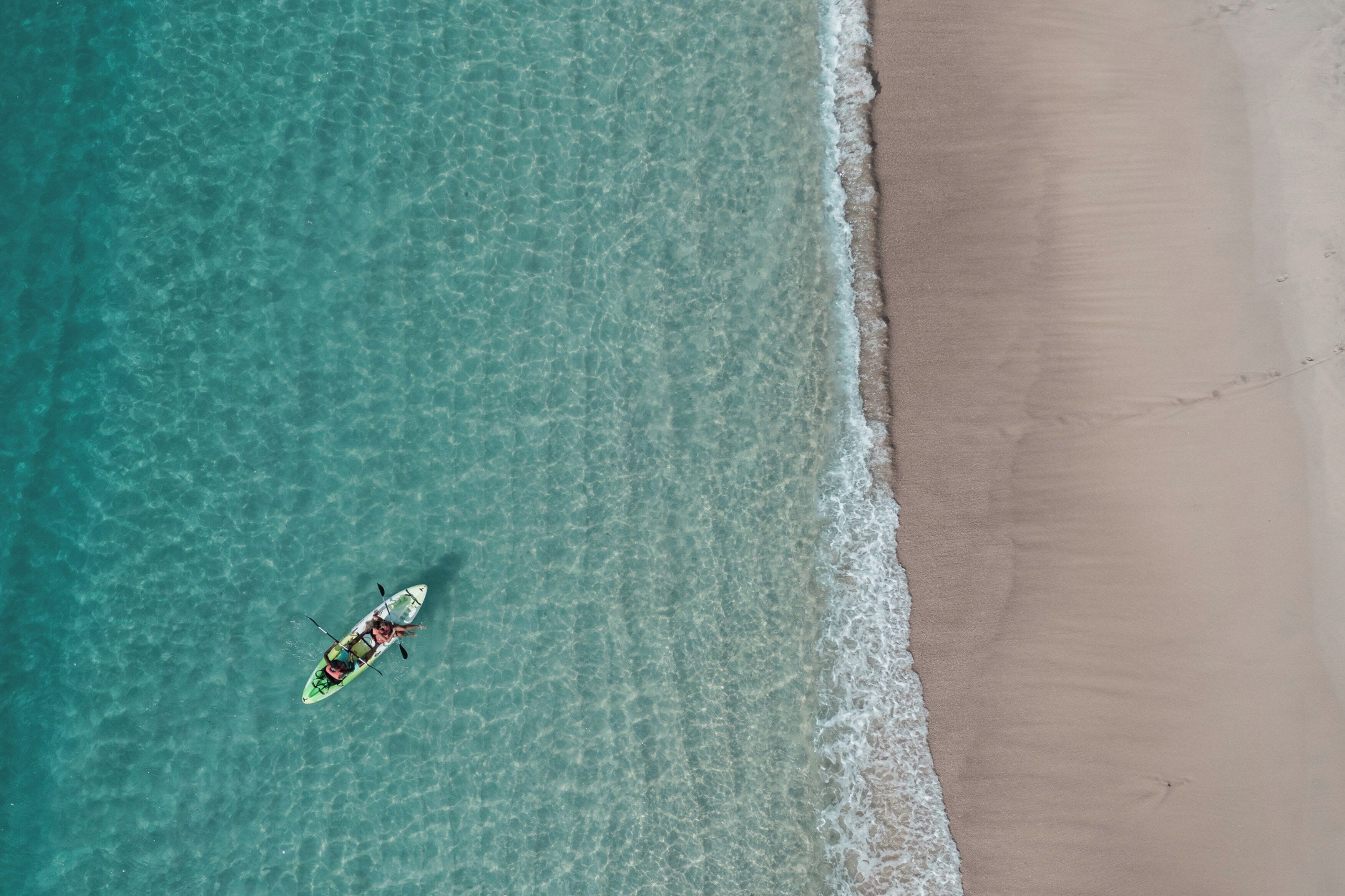 Vue aérienne d’une plage aux eaux turquoise et limpides, bordée d’un rivage sablonneux.