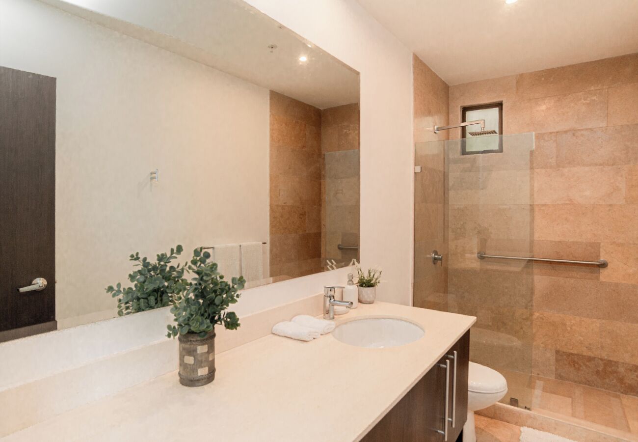 A modern bathroom with a large mirror, a sink, a shower, and a potted plant.