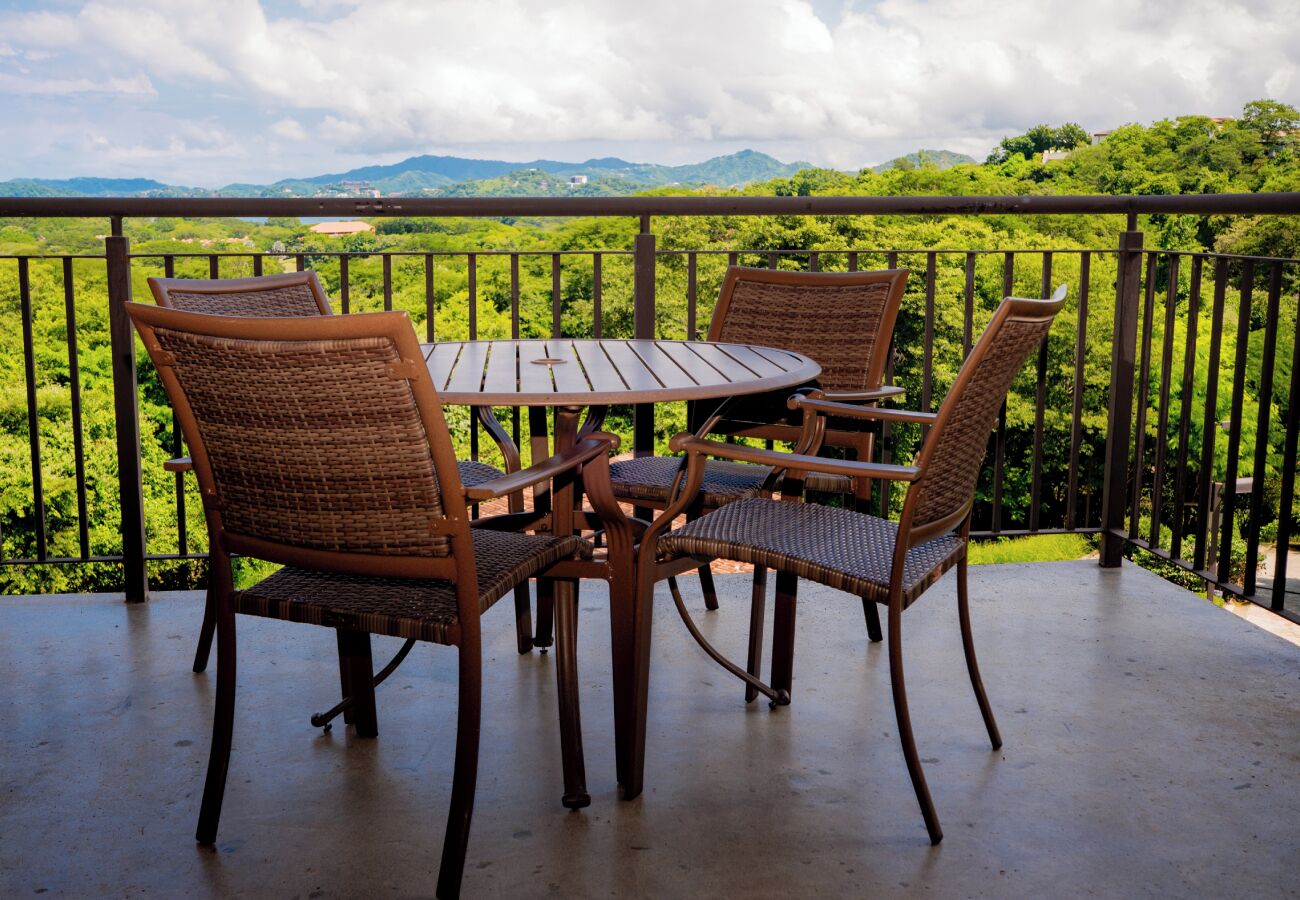 Eine Terrasse mit Korbstühlen und einem Holztisch, mit Blick auf eine üppige, grüne Landschaft und Berge in der Ferne.