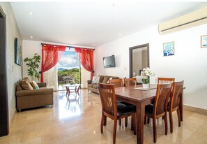 A spacious living area with a dining table and chairs, a sofa, and a TV mounted on the wall. - Reserva Conchal Resort - Roble Sabana Complex (Cabo Velas)