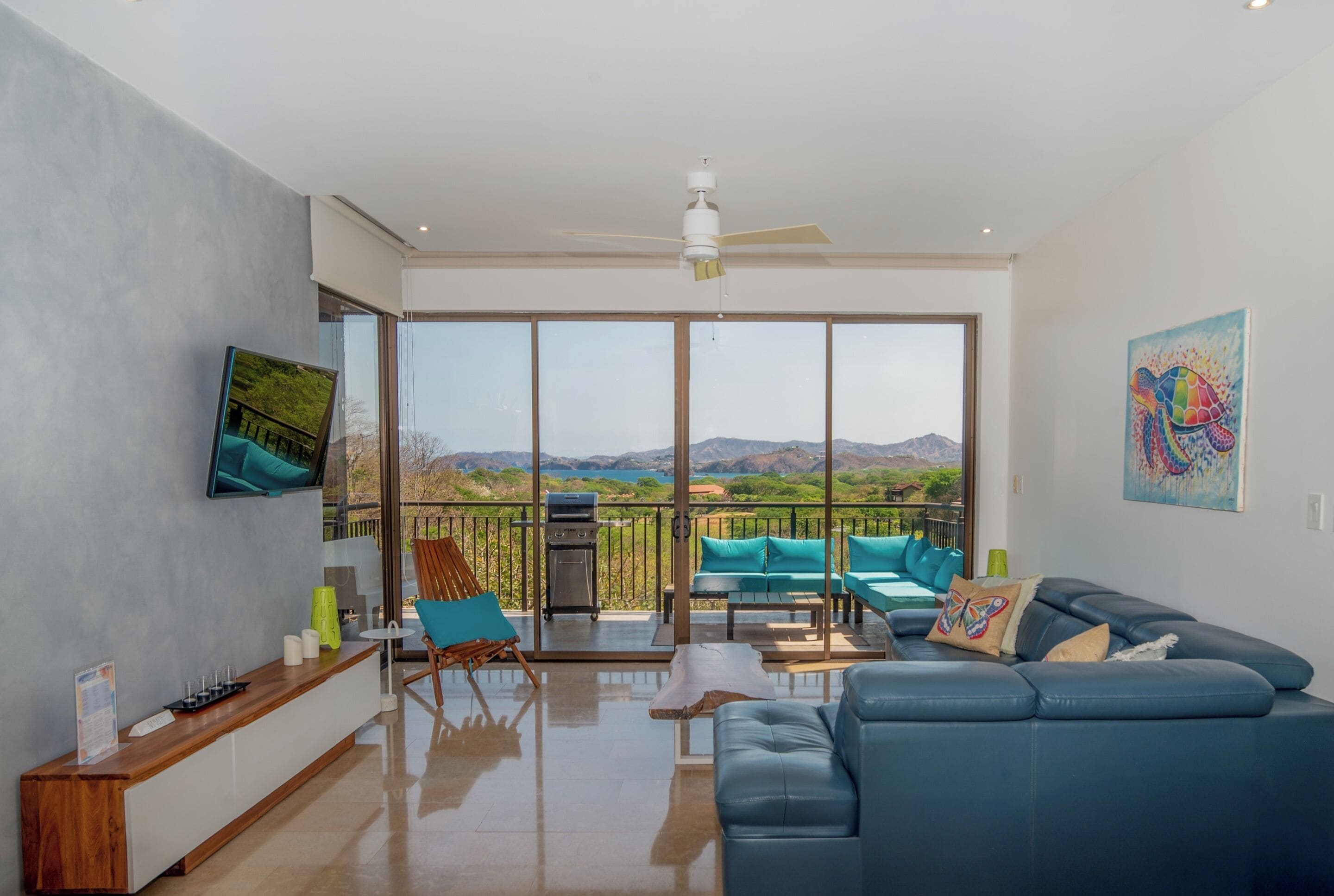A spacious living area with a blue sofa, teal chairs, and a large window offering a mountain view.