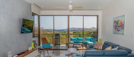A spacious living area with a blue sofa, teal chairs, and a large window offering a mountain view.