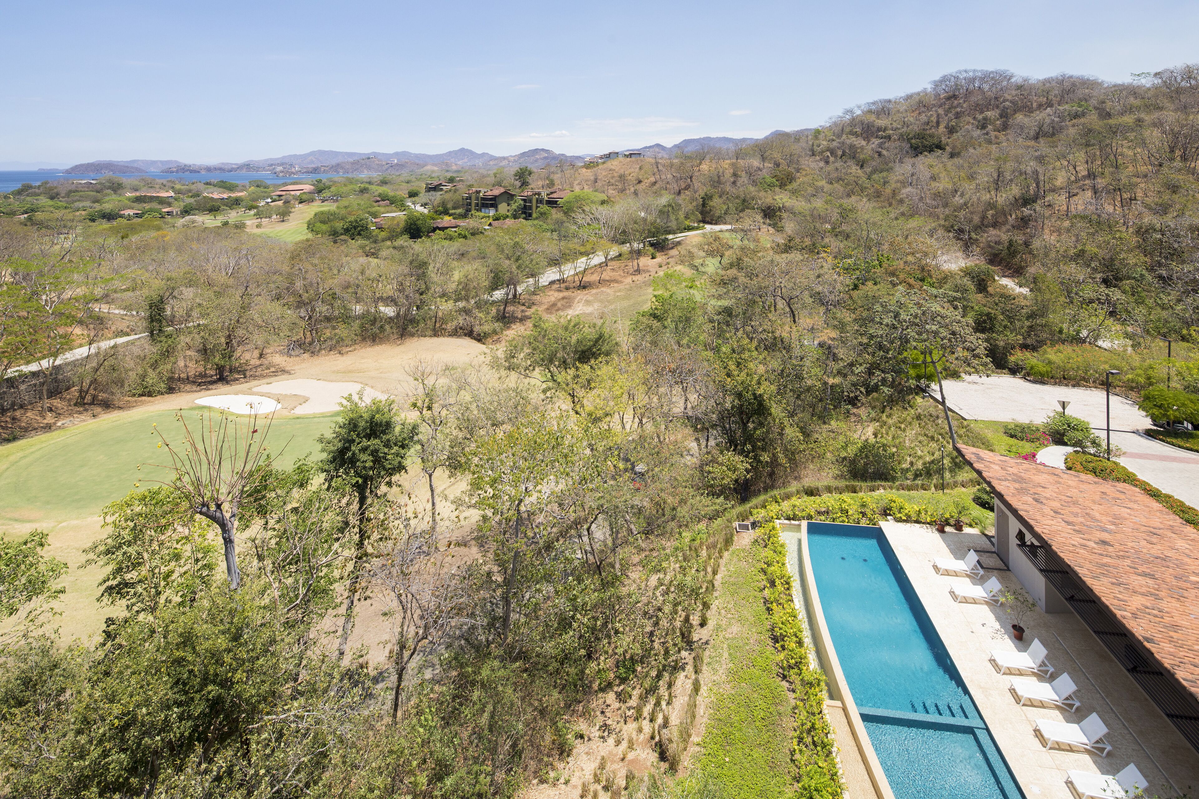 A pool with lounge chairs, a golf course, and a hilly landscape.
