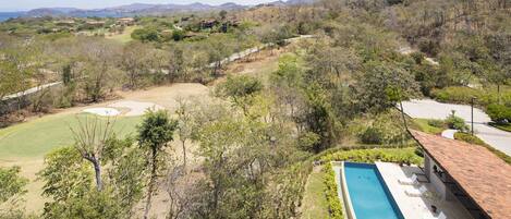A pool with lounge chairs, a golf course, and a hilly landscape.