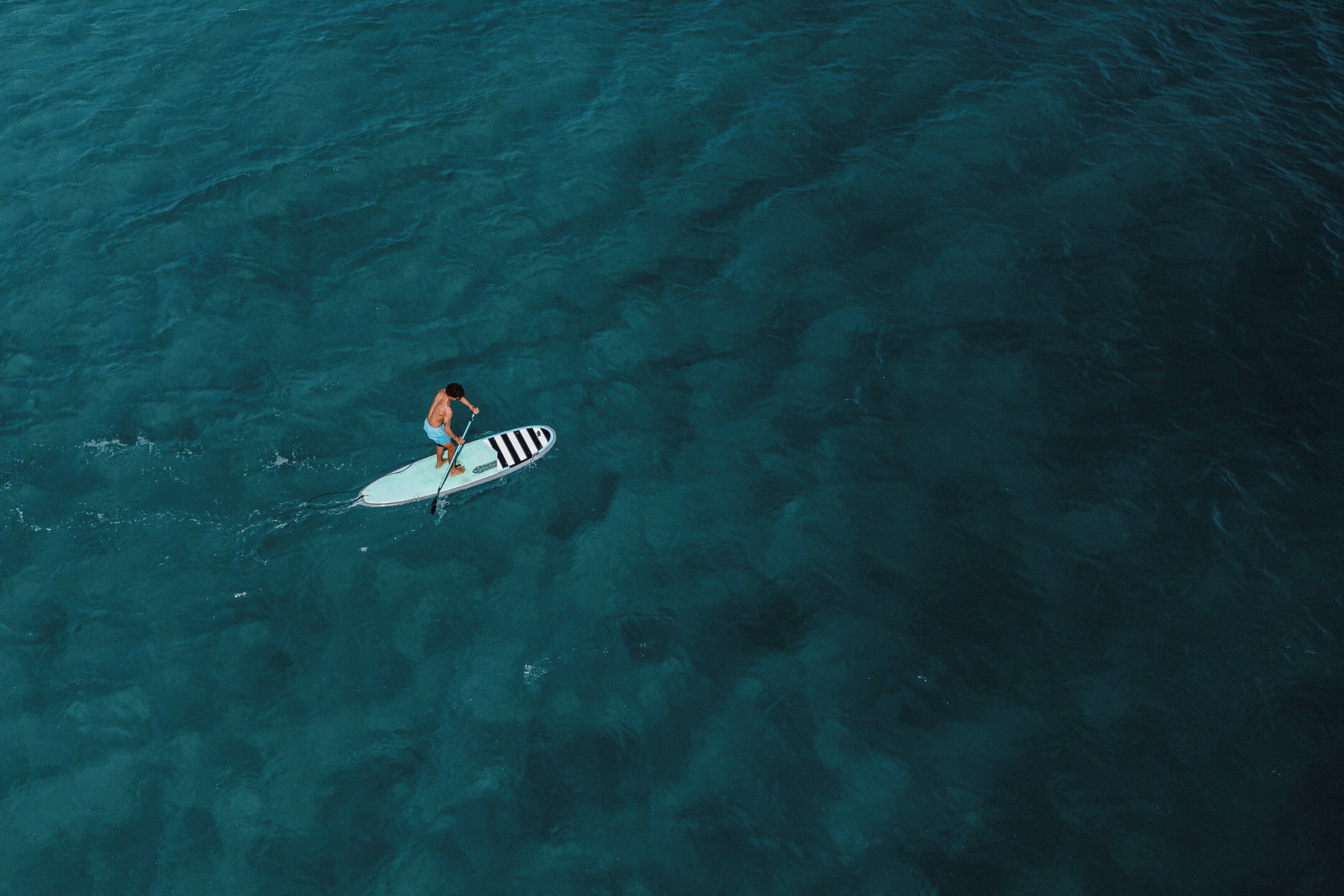 Uma pessoa remando em uma prancha de surf em águas extensas.