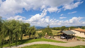Een landgoed op het platteland met een stenen terras, buitenmeubels en uitzicht op glooiende heuvels.
