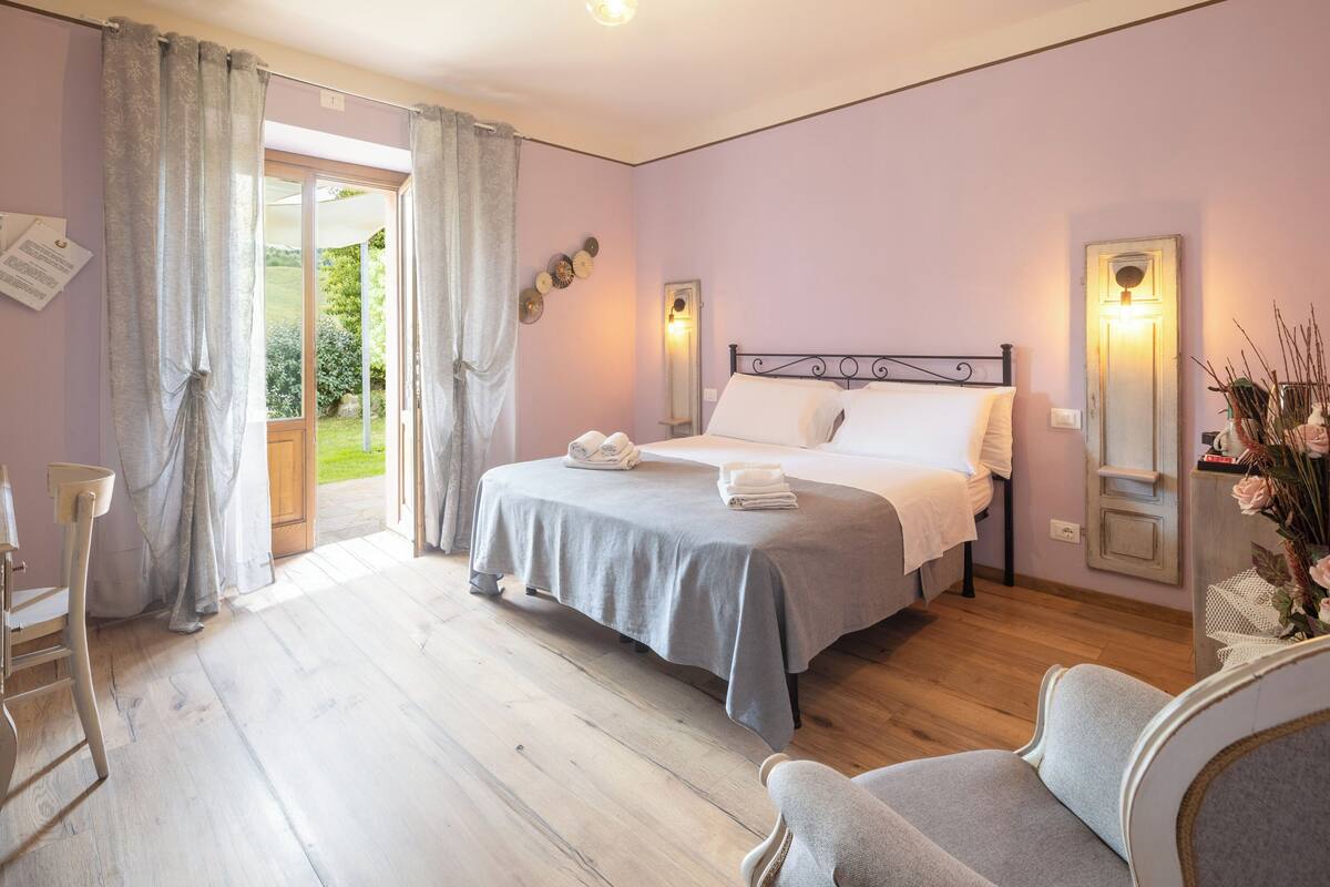 Une chambre à coucher avec un lit, une chaise, une table de chevet et une fenêtre avec des rideaux.
