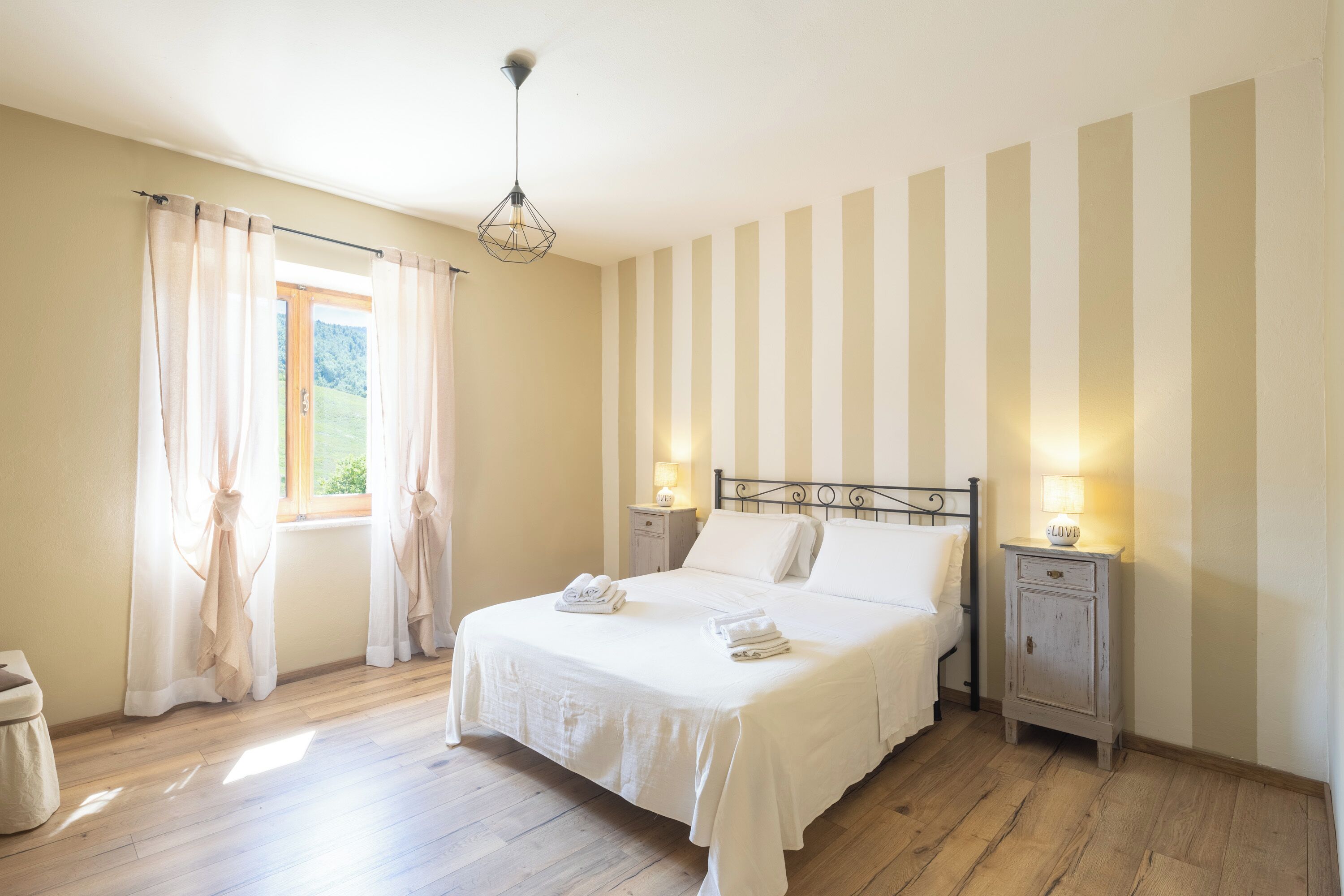 Una camera da letto con un letto, due comodini, una finestra con tende e una lampada a sospensione.