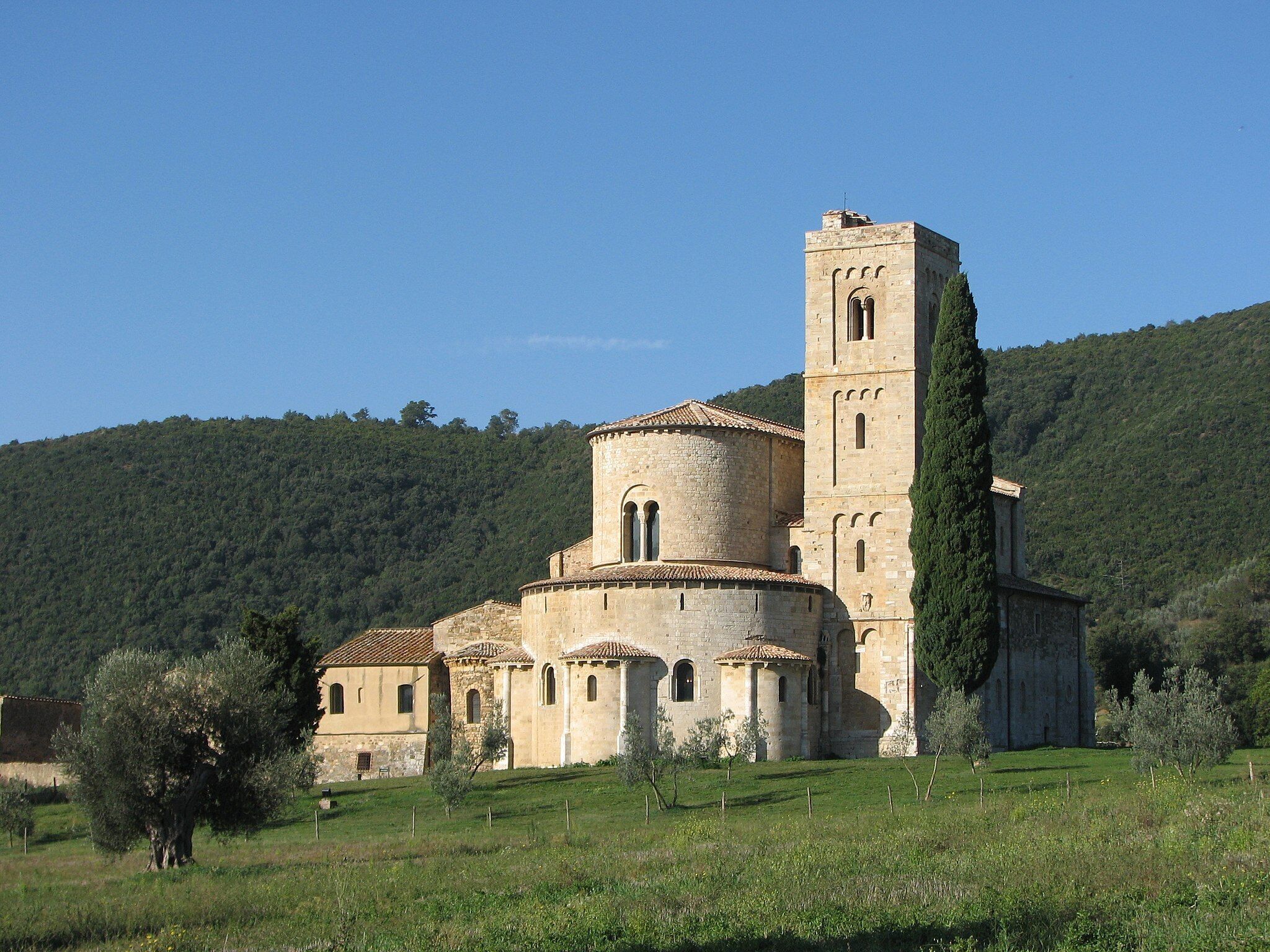A historic church with a bell tower, surrounded by a grassy field and a forested hill.