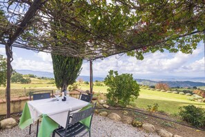 Un espace extérieur aménagé pour les repas, avec une table et des chaises, une pergola et une vue sur un paysage rural.