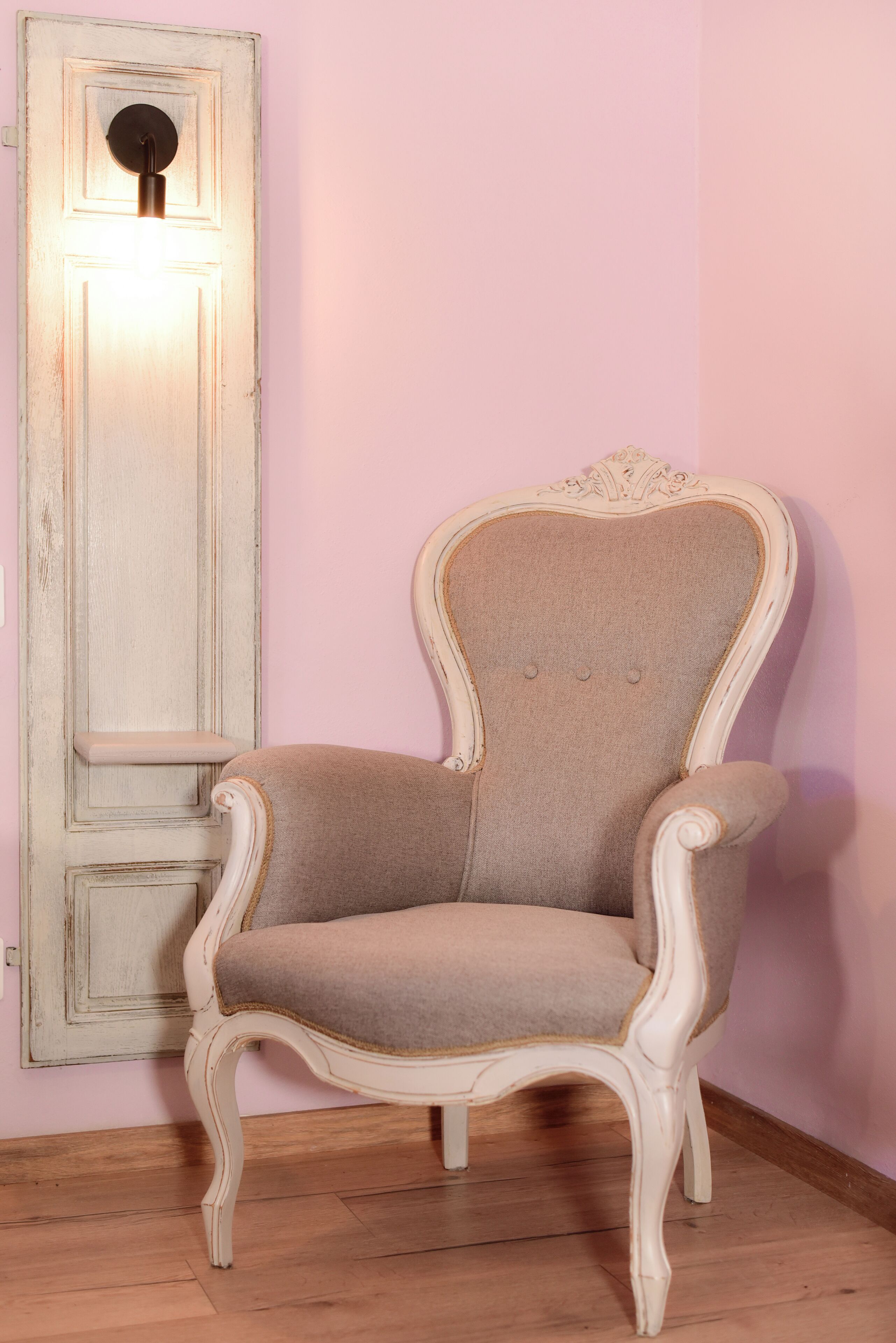 Une chaise dotée d’un haut dossier et d’accoudoirs, placée contre un mur où se trouvent un interrupteur et une porte.