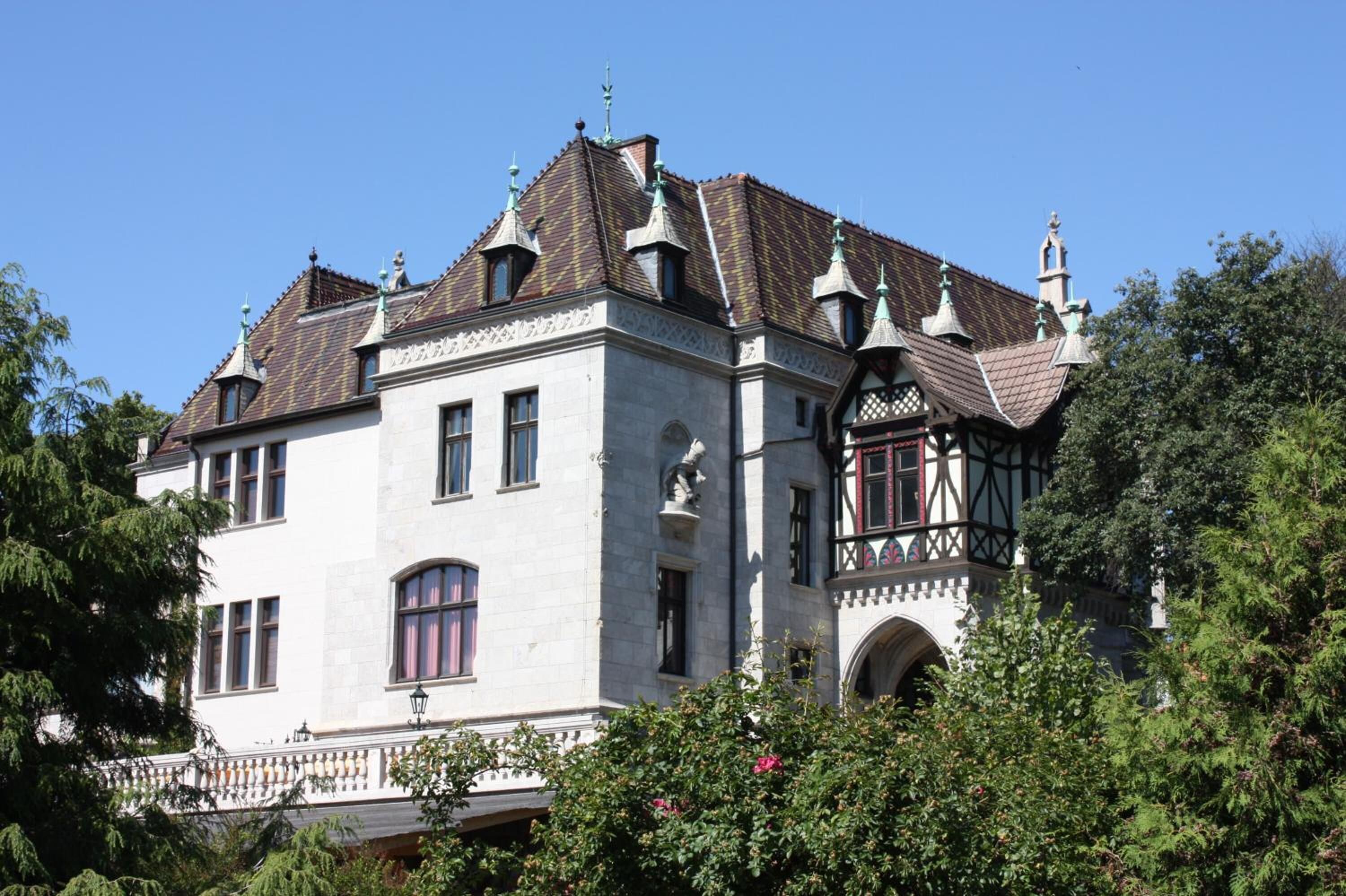 Een groot, historisch gebouw met een symmetrische gevel, meerdere ramen en een toren met een puntige torenspits.