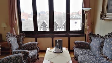 Una habitación con dos sofás decorados, una mesita y vistas a edificios a través de amplios ventanales.