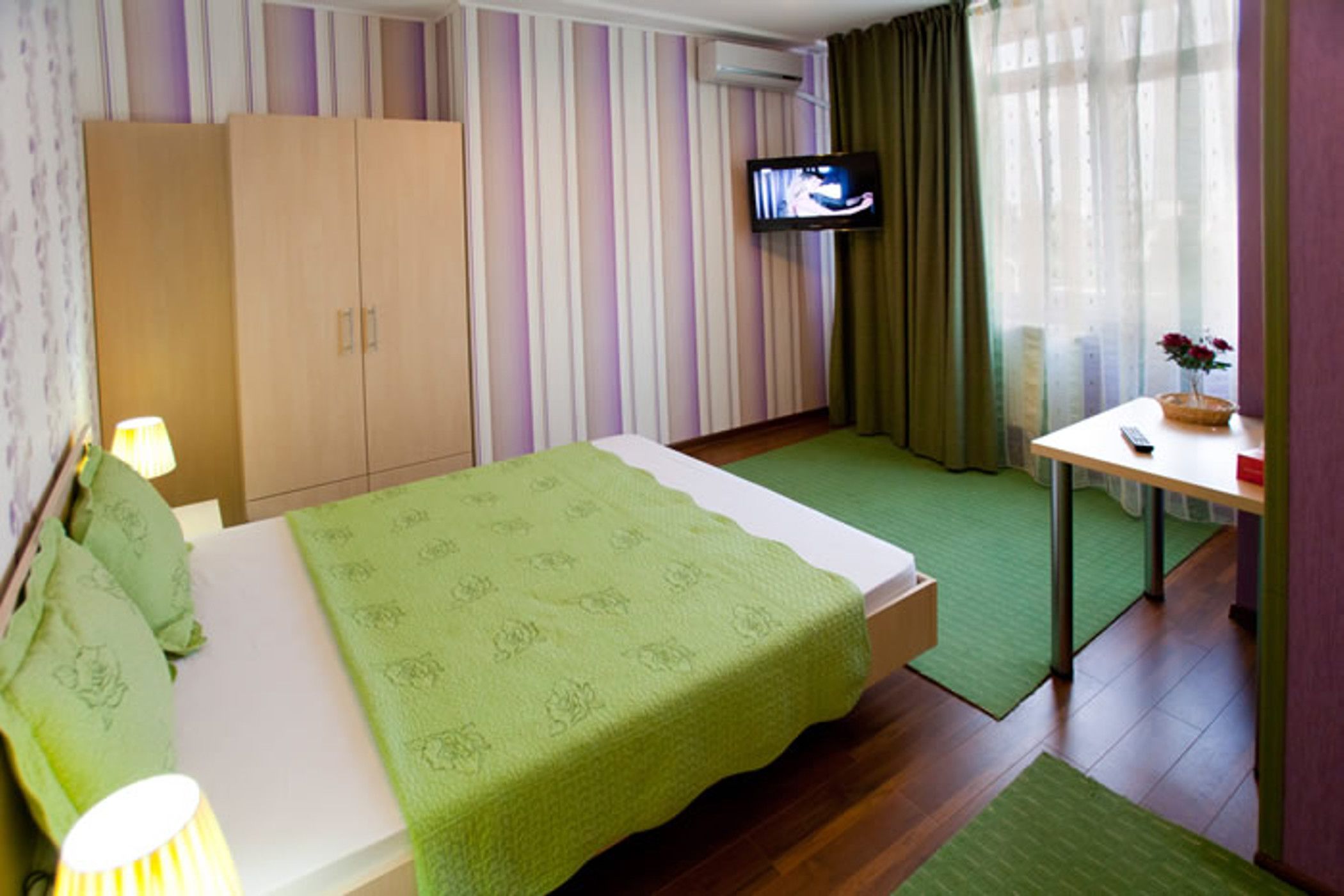 A hotel room with a bed, a television, a desk, and a window with curtains.