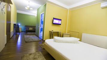 Habitación de hotel con cama, televisión montada en la pared y un pasillo que conduce a otra habitación.