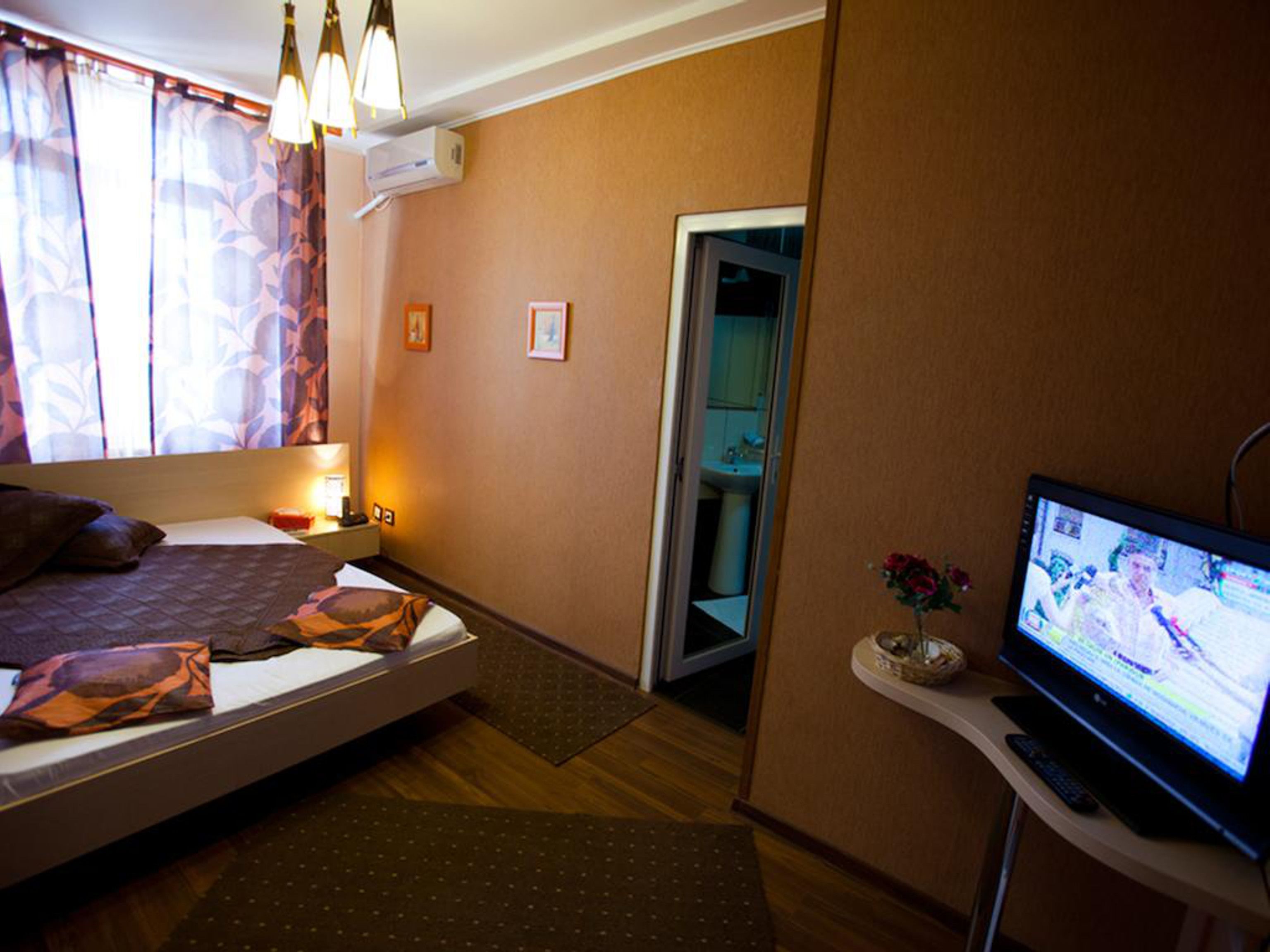Quarto de hotel com cama, mesa de cabeceira, luminária, televisão e banheiro visível por uma porta aberta.