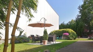 Un espace extérieur aménagé en terrasse, avec une table et des chaises, un grand parasol et une sculpture en pierre.