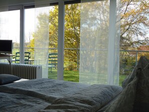 A bedroom with a large window, a bed, a radiator, and a television on a stand. - Haus Tourneur (Lippetal)