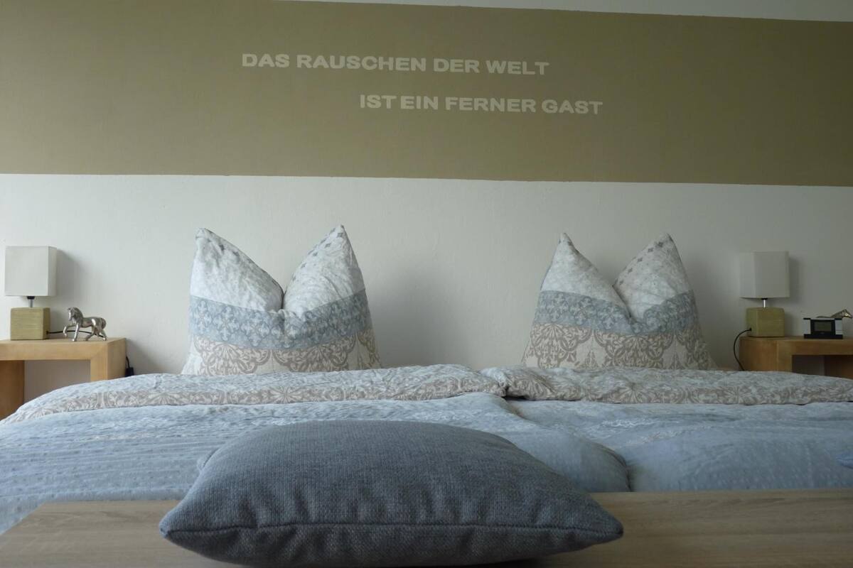 A bedroom with a bed, pillows, and a wall-mounted text.