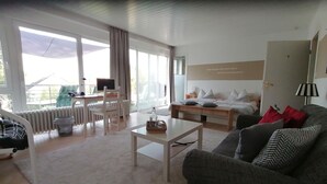 Une chambre d’hôtel moderne dotée d’un grand lit, d’un canapé, d’un bureau avec un ordinateur et offrant une vue sur l’extérieur.