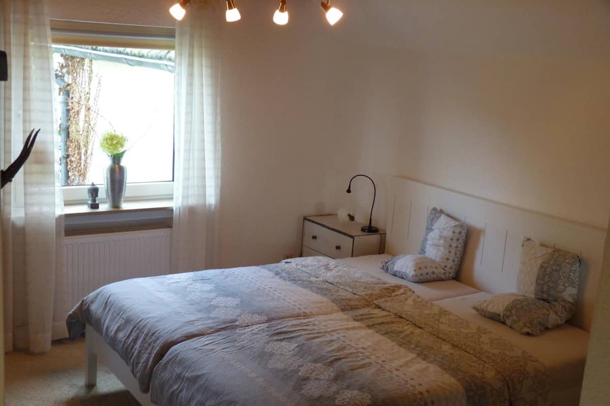 A bedroom with a large bed, a bedside table, a lamp, and a window with curtains.