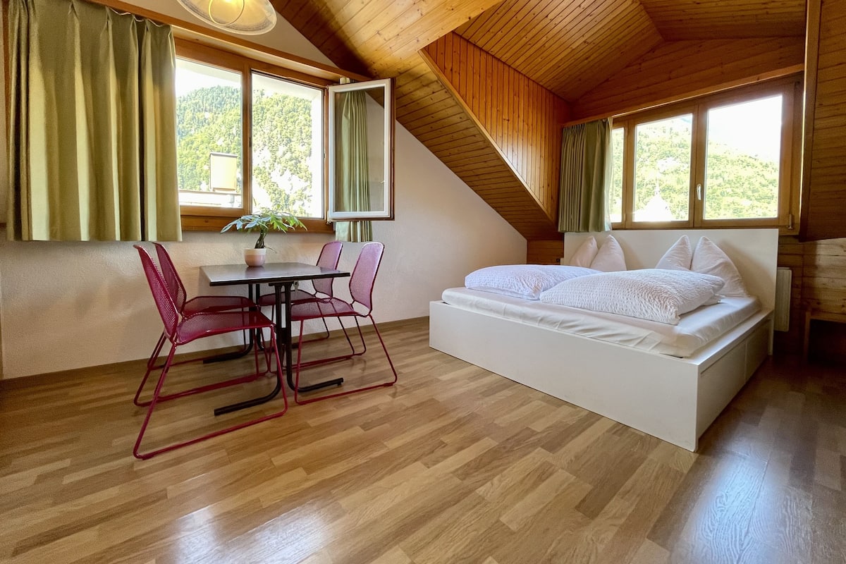 A cozy room with a loft bed, wooden ceiling, and large windows.