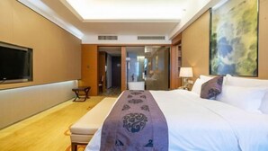 Habitación de hotel con una cama grande, un televisor de pantalla plana montado en la pared, una mesita de noche y un ventanal amplio.