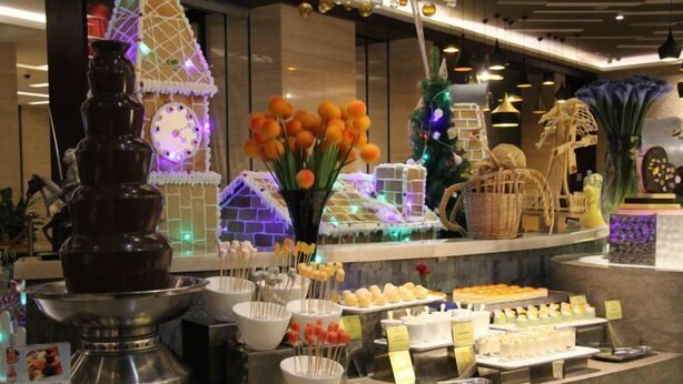 Zona de bufé con una variedad de alimentos, una casita de jengibre decorativa y una fuente de chocolate.