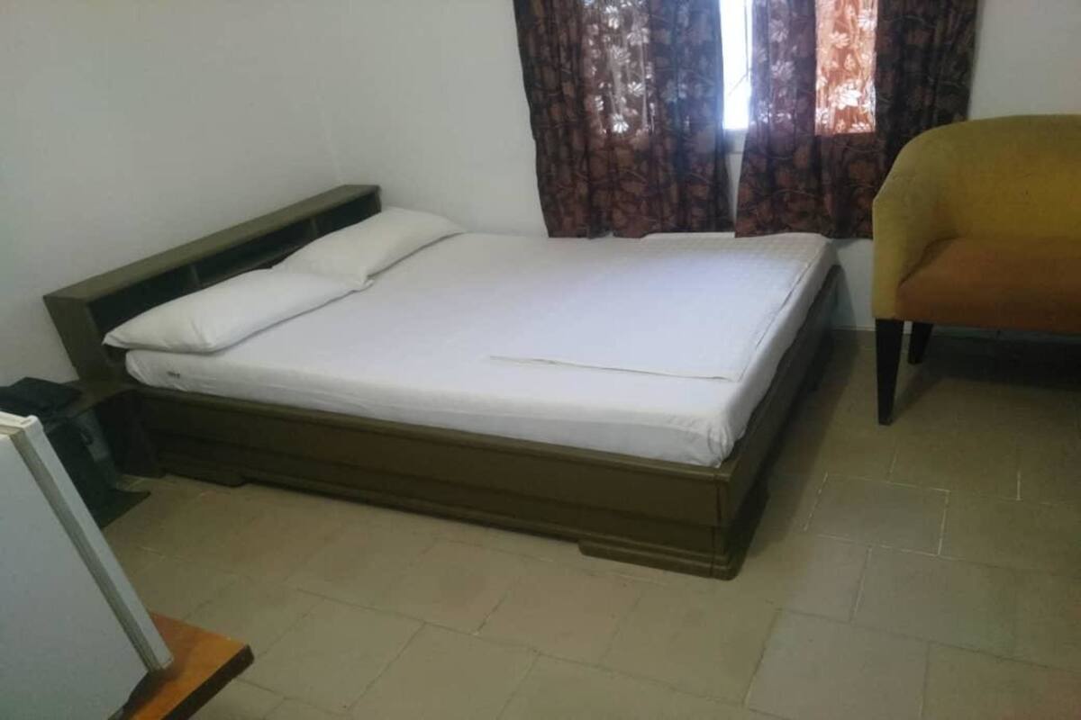 A single bed with a wooden frame and white bedding in a room with a tiled floor.