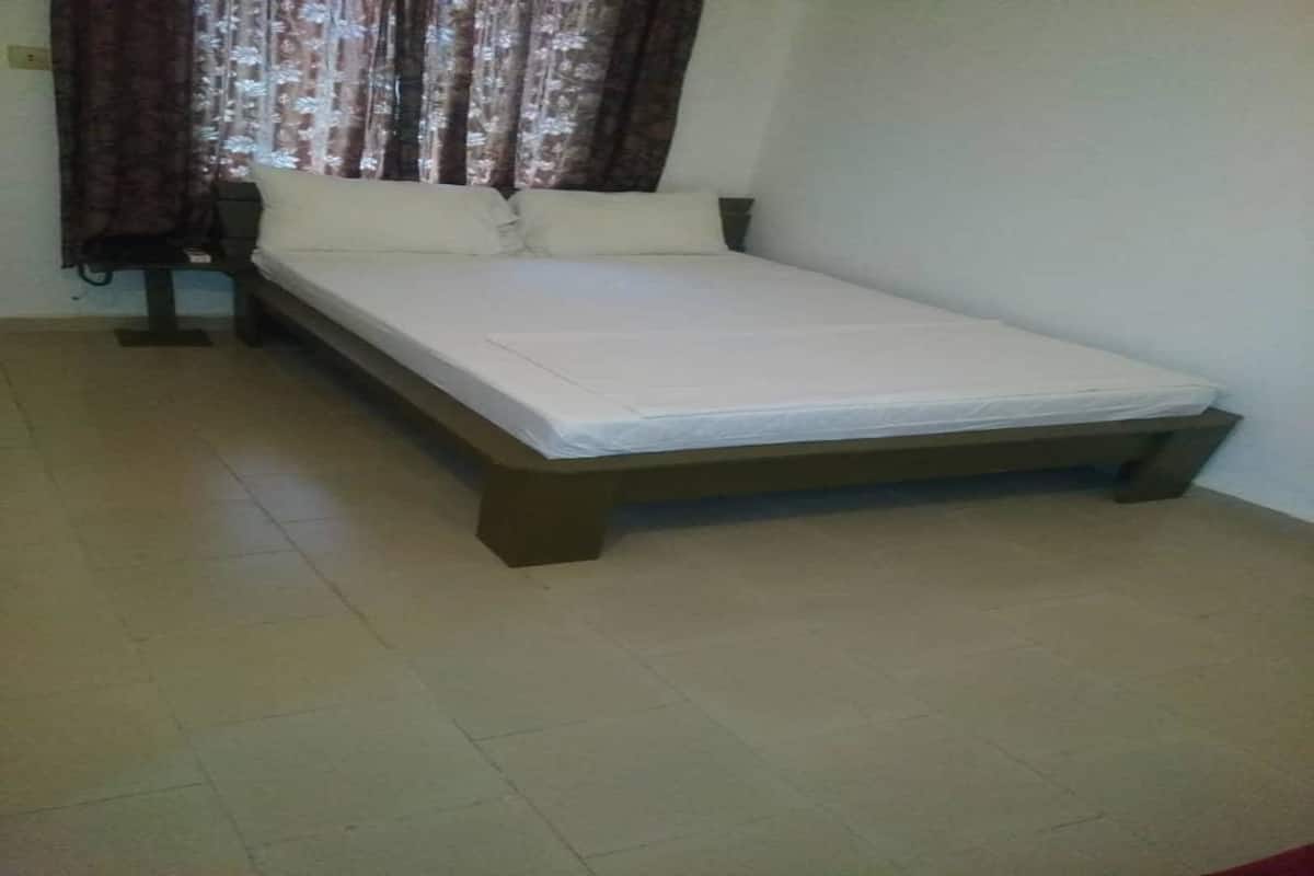 A single bed with a wooden frame and white bedding in a room with tiled flooring and a curtain on the window.