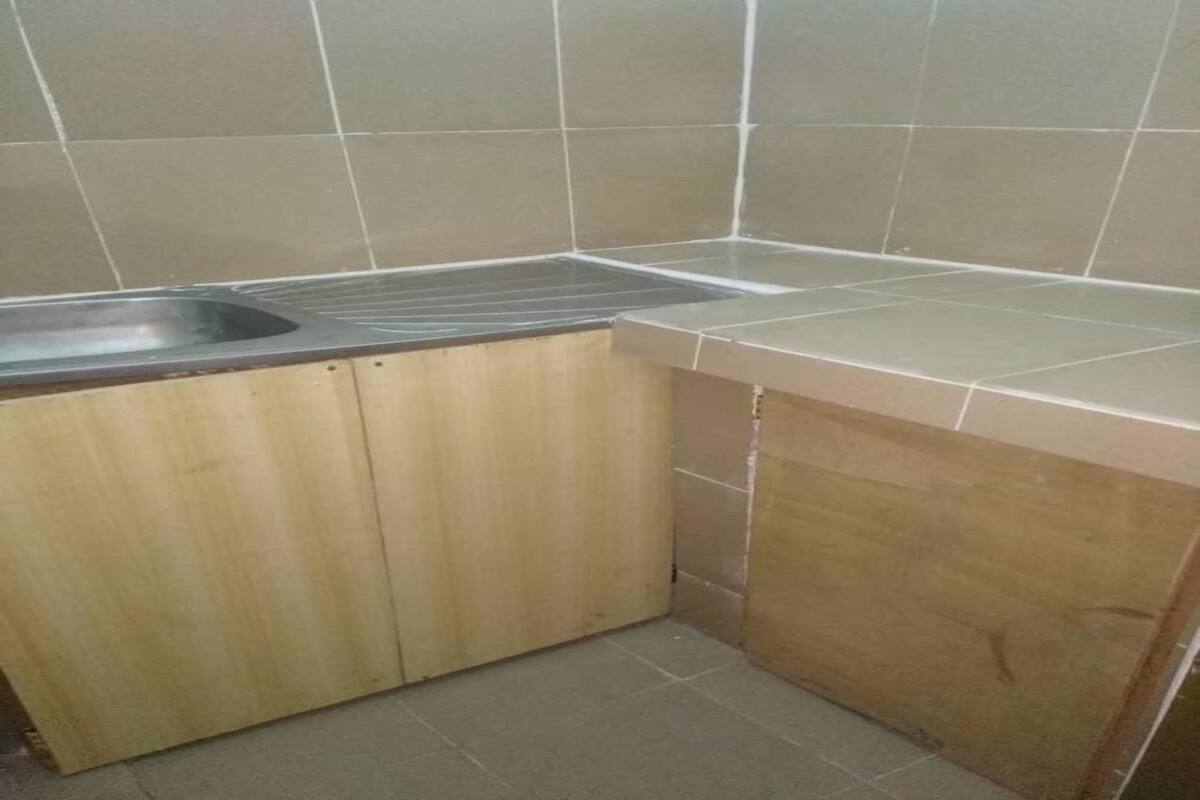 A small kitchen with a sink, wooden cabinets, and tiled walls.