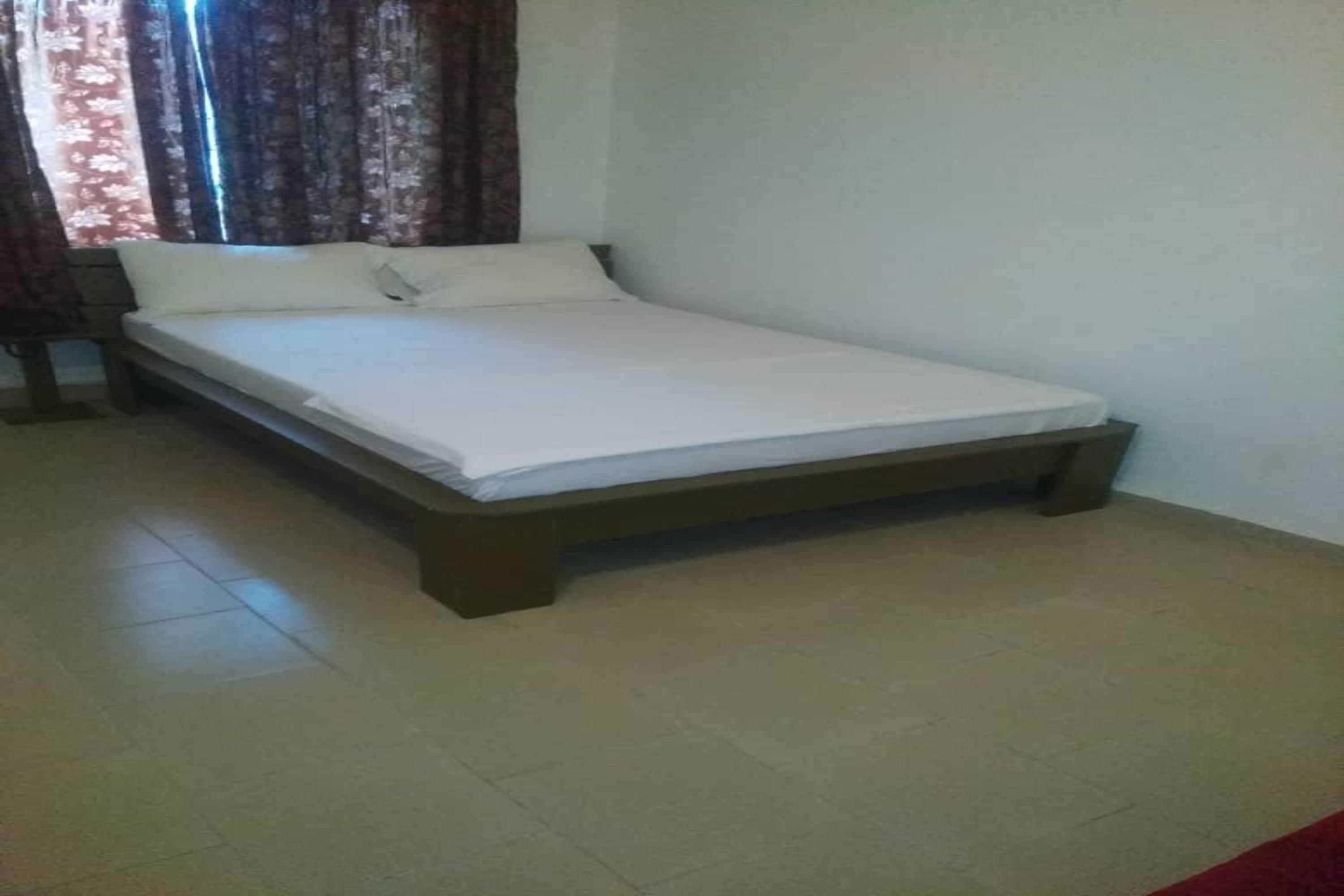A single bed with a wooden frame and white bedding in a room with tiled flooring and a plain wall.