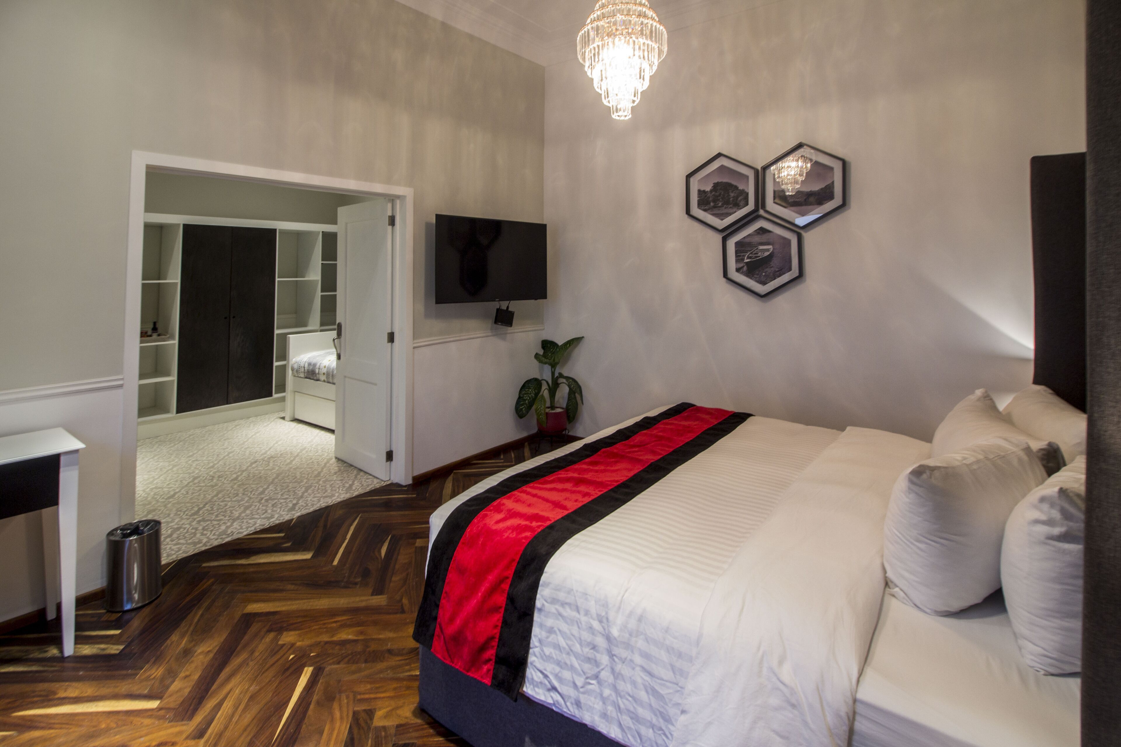 Ein Schlafzimmer mit einem großen Bett, einem an der Wand montierten Fernseher, einer Pflanze und einer Kristallleuchter.