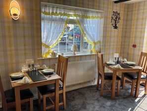 A dining area with a table set for four, a window with curtains, and a radiator below. - The Glenwood (Torquay)