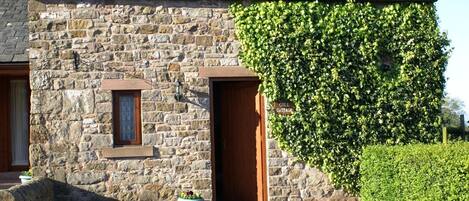 A stone cottage with a wooden door, a small window, and a sign reading "GILL COTTAGE".