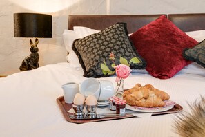 Una cama bien tendida con almohadas, una bandeja con artículos para el desayuno y una lámpara decorativa.