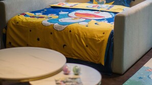A room with a bed featuring a Doraemon-themed bedspread and pillow. There is a small round table with a white surface and a few items on it. - Novotel Nantong Center (Nantong)