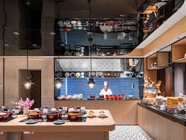 Una cocina moderna con un chef preparando comida, una variedad de platos expuestos y una distribución limpia y ordenada.