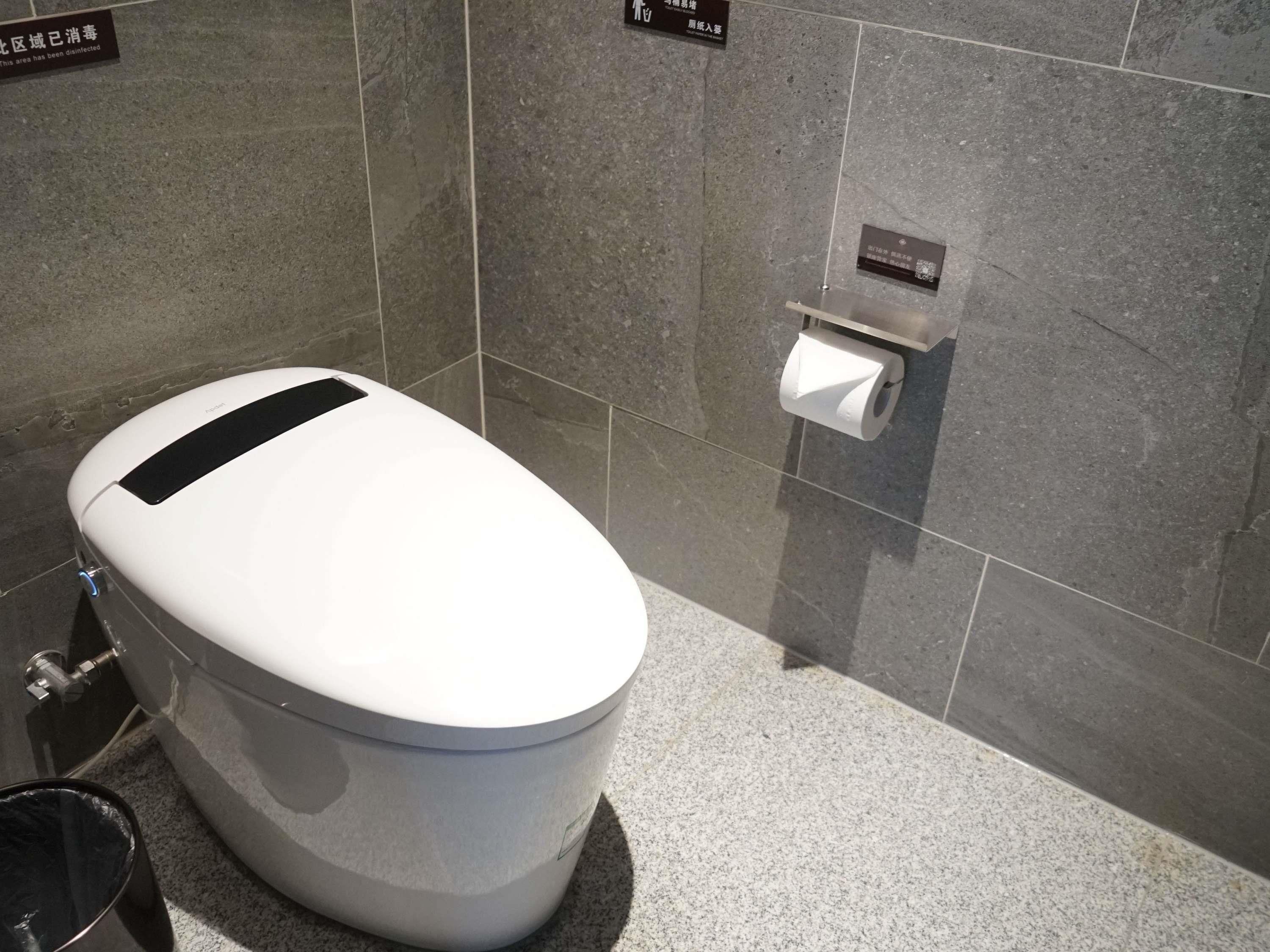 A modern bathroom with a white toilet, a trash bin, and a toilet paper holder on the wall.