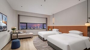 A modern hotel room with two beds, a seating area, a large window with a city view, and a small table with a vase of flowers. - Novotel Nantong Center (Nantong)