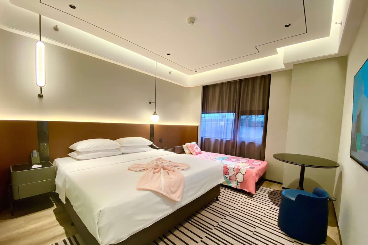 Ein Hotelzimmer mit einem großen Bett, Nachttischen, einem Schreibtisch, einem Sessel und einem kleinen runden Tisch, sowie einem Fenster mit Vorhängen.