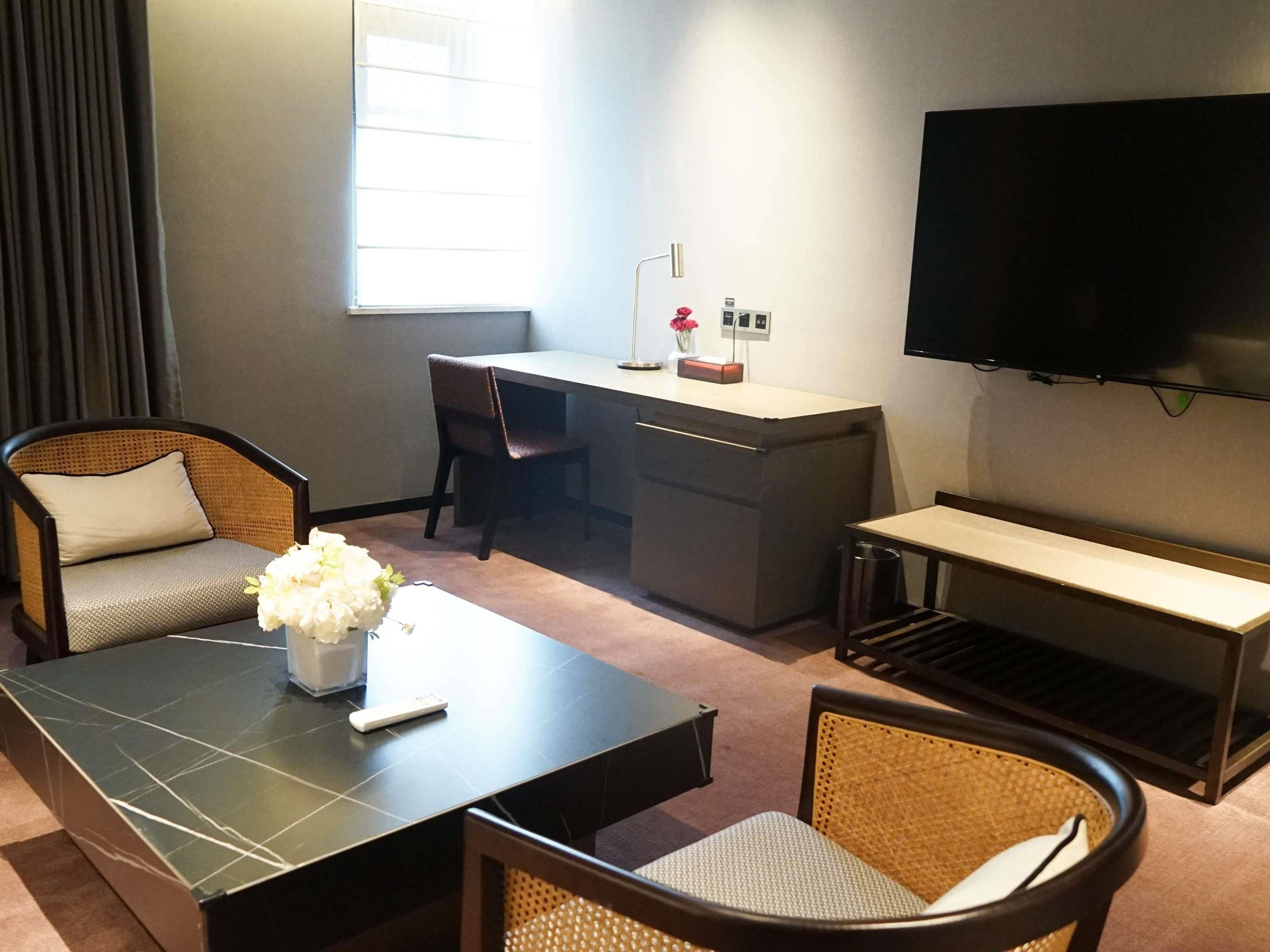A hotel room with a sofa, a dining table, a TV, a desk, and a trash bin.