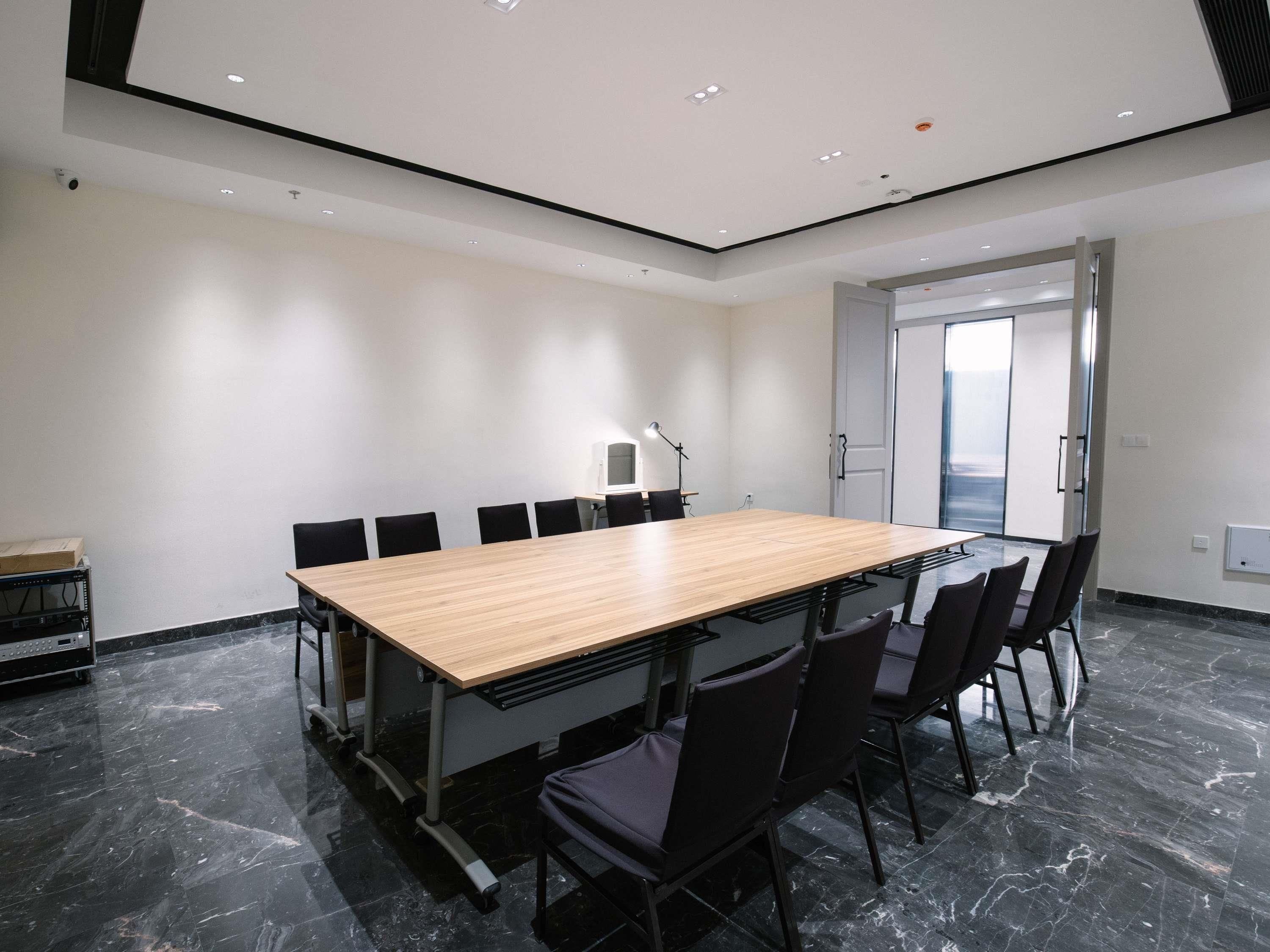 A conference room with a long table, chairs, a desk with a computer, and a door leading outside.