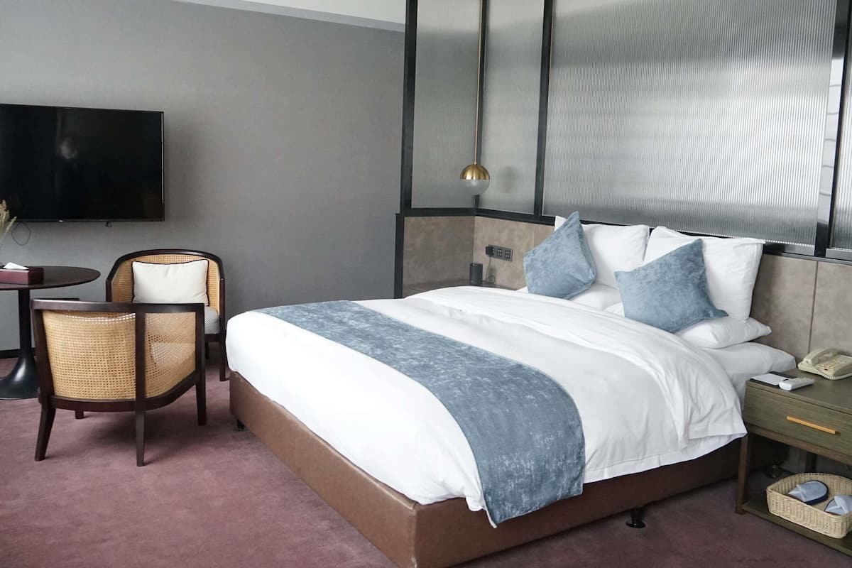 Ein Hotelzimmer mit einem großen Bett, einem Schreibtisch mit Stuhl, einem Fernseher und einem Nachttisch mit Telefon und Korb.