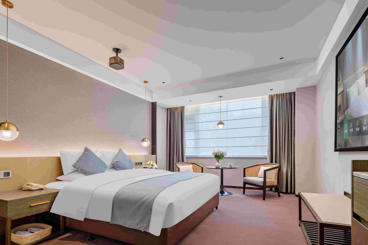 Ein Hotelzimmer mit Bett, Nachttisch, Lampe, Sessel und einem kleinen Tisch mit einer Vase.