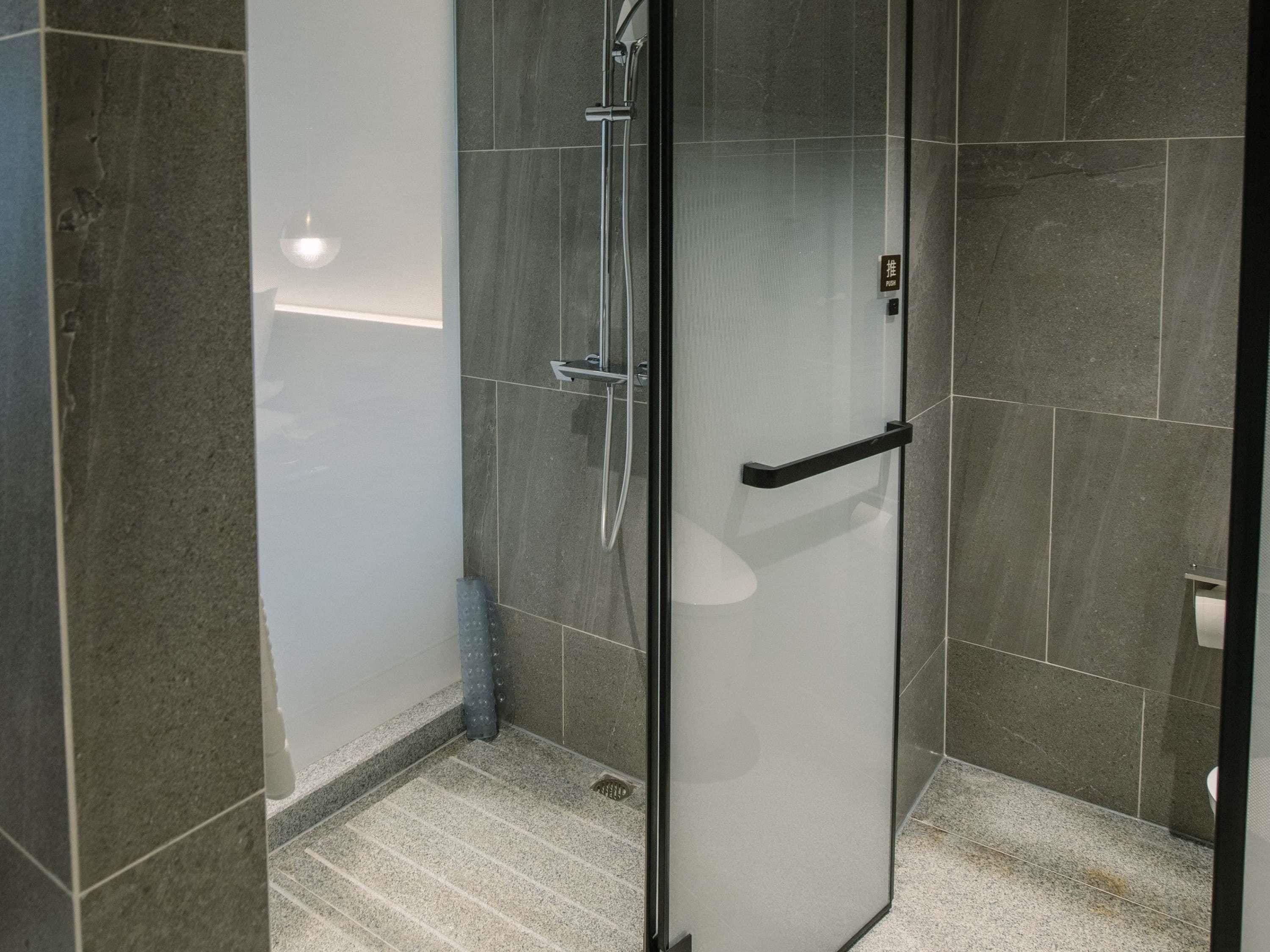 Een moderne badkamer met een douchecabine van glas, een zwarte handdoekhouder en grijze betegelde wanden.