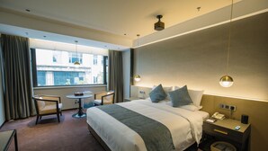A hotel room with a bed, bedside table, lamp, chair, and a view of the outside. - Novotel Nantong Center (Nantong)